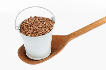 Full bucket of buckwheat grains stands in a wooden spoon.