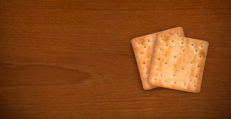 Fresh baked cream crackers in two pieces isolated on dark teak wood background with copy space for text decoration