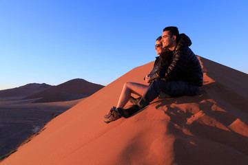 Couple on sand dune in desert during sunrise.  Sossusvlei, Namib Naukluft National Park, Namibia