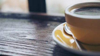 Closeup image of yellow hot coffee cup on vintage wooden table in cafe