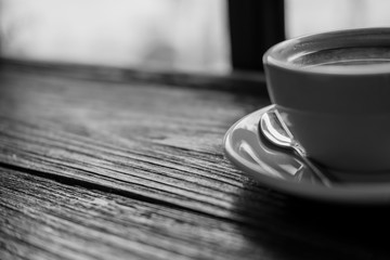 Black and white image of hot coffee cup on vintage wooden table in cafe