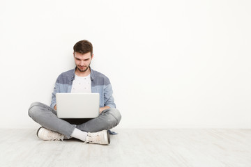 Young man working on laptop sitting on floor