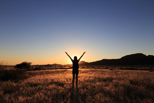 Silhouette of woman open arms under the sunset at african savanna landscape.