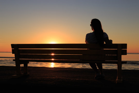 The silhouette of a lonely girl sitting on a bench watching the sunset