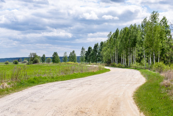 a ground winding road between fields and trees under Cumulus clouds in summer