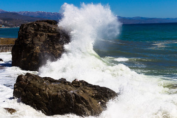 Crimea. Alushta. Sea. The wave beats against the rock and spreads out with splashes. Bright blue sky and mountains.