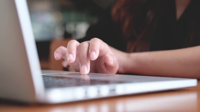 Closeup image of a business woman's hands pressing and sliding on laptop keyboard on wooden table in office