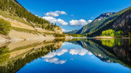 Naklejka na ściany i meble Reflections of blue sky, trees and mountains in the smooth surface on the crystal clear water of Crown Lake, along Highway 99 in Marble Canyon Provincial Park in British Columbia, Canada