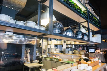 Photo sur Aluminium brossé Restaurant Restaurant kitchen interior: bar counter made of natural stone, fences off the open kitchen and hall for visitors with tables and chairs. In the background buzzing restaurant work motion chefs
