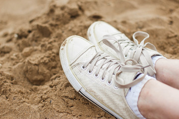 Stylish white sneakers on sand background close up.