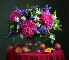 Bouquet of cultivated flowers in the jug and peaches.