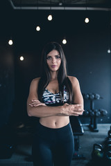 Beautiful young fit woman stretching and posing in fitness gym. Low light scene.