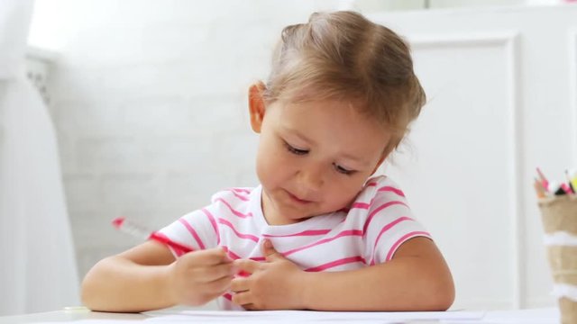 Cute preschool girl sitting by the white table focused on drawing something.