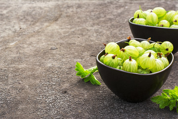 Fresh green gooseberries in a ceramic bowl on a dark background. Top view