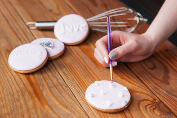 Gingerbread decorated with icing by female baker. Sweet dessert on woooden background, colorful cookie, wedding present closeup. Tasty food, bakery concept
