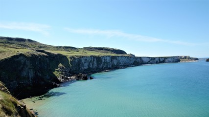 Obraz premium Long shot over the coastline at the Carrick-a-Rede coastal walk to the rope bridge in County Antrim, Northern Ireland, UK