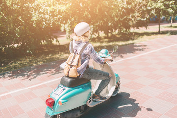 Fototapeta premium Młoda wesoła dziewczyna jazdy skuterem w mieście. Portret młodej i stylowej kobiety z motorowerem.