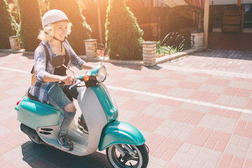 Naklejka premium Młoda wesoła dziewczyna jazdy skuterem w mieście. Portret młodej i stylowej kobiety z motoroweru.