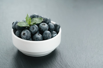 fresh blueberries with mint leaves in white bowl on slate board