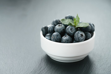 fresh blueberries with mint leaves in white bowl on slate board