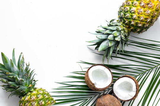 Concept of summer tropical fruits. Pineapple, cocount and palm branch on white background top view copyspace
