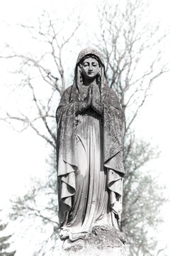 The old figure of the Virgin Mary, who prays in a cemetery (black and white concept)