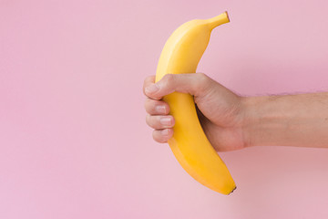 Male hand holding a banana isolated on pink background.