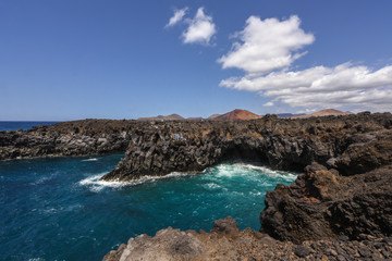 Los Hervideros lava cave in the turquoise sea with volcano in the background - the unique volcanic landscape of Lanzarote and popular touristic attraction, Canary islands, Spain