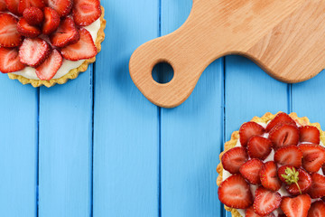 Two homemade tarts with fresh organic strawberries and wood cutting board on blue table copyspace