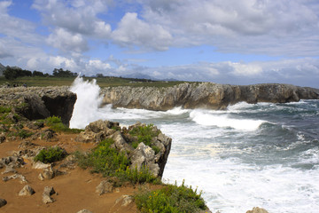 blue sky and waves splashing against a cliff in Pria, Spain