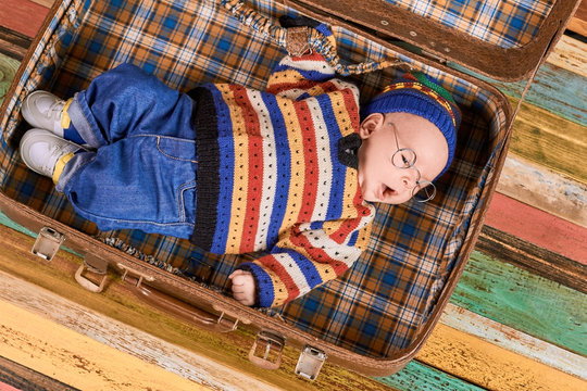 Baby lying in opened suitcase. Little kid wearing spectacles. Smart travel strategies.