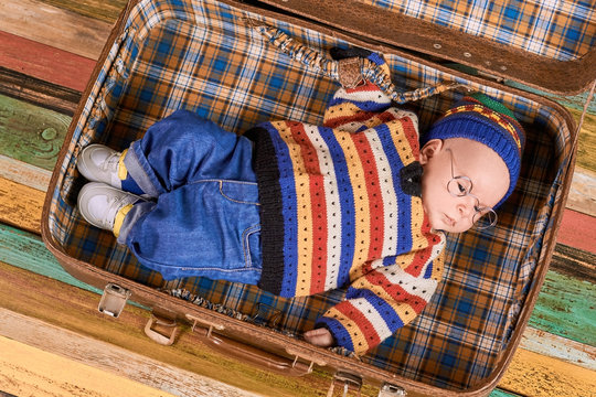 Baby lying in suitcase. Small child wearing spectacles.