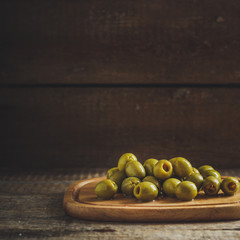 Olives on a wooden board on a dark woody background