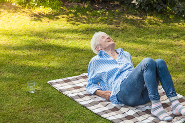 Lebenslustige Seniorin liegt auf karierter Decke im Garten und lacht schallend