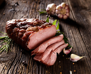 Smoked ham sliced  on a wooden rustic table with addition of fresh aromatic herbs and spices, natural product from organic farm, produced by traditional methods