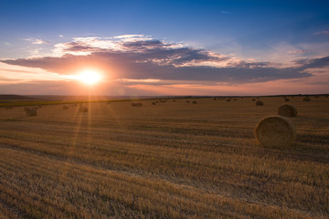 The field with round haystacks and the sun with rays between the clouds
