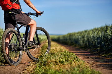 Fototapeta na wymiar Close-up of cyclist man legs with mountain bike on the path of the green field in the countryside.