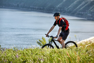 Attractive cyclist rirding mountain bike above beautiful river in the field in the countryside.