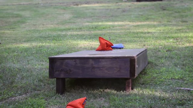 Cornhole bags land on cornhole board in summer at backyard party