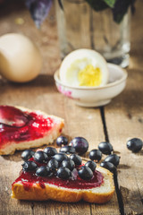  Breakfast on a wooden background: sandwich with jam, eggs, basil, tea