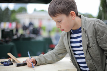 Young boy draw layout on the wooden desk. Classes for young carpenter cutting wooden board form using fretsaw. Toy making. Dreaming of future profession. child woodcarving lessons