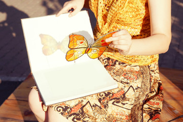 Handmade stained glass butterfly in woman's hands, color reflection on the book