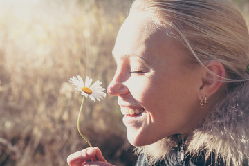 Happy woman smelling daisy flower hanging it in hands