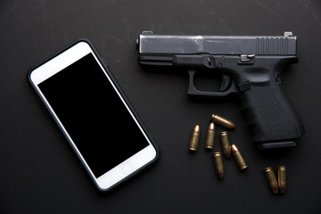 Gun with ammunition and mobile phone on black background. top view
