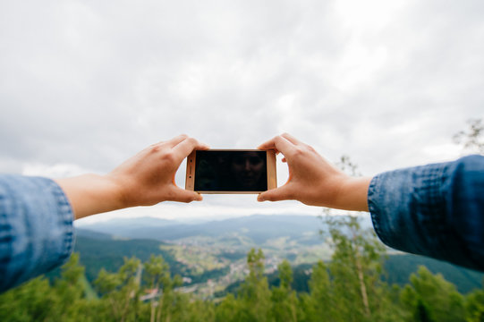 Closeup of tan women hands holding mobile phone with wide touchscreen and making photos and video of beautiful nature landscape from high altitude in mountains.  Low cloudy sky. Travel and dicover.