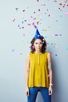 Ruined Party. Sad Young Woman Standing And Looking At Camera With Birthday Hat And Confetti Around Her