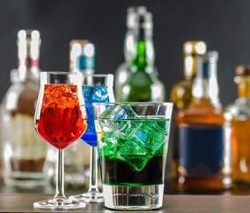 Colorful drink on the background of bottles in original shapes, cocktail drink with ice cubes