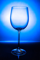 Empty wine glass with reflection on a blue background with a gradient spot
