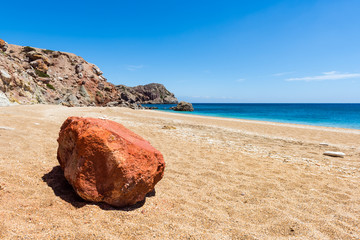 The volcanic rock colored in vivid red on sandy Paleochori Beach. Milos. Cyclades Islands, Greece.