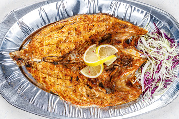 Grilled sea bream fish on foil plate served with lemon and cauliflower